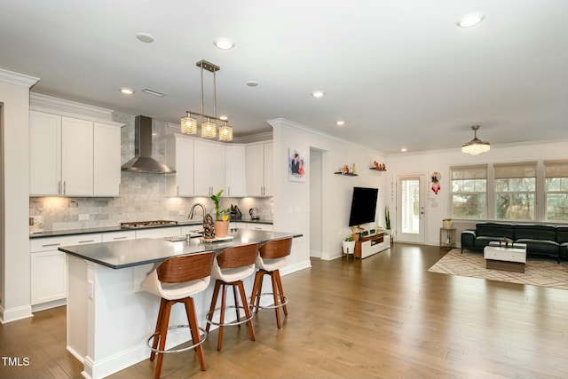 kitchen featuring wood-type flooring, a kitchen island with sink, white cabinets, and wall chimney exhaust hood