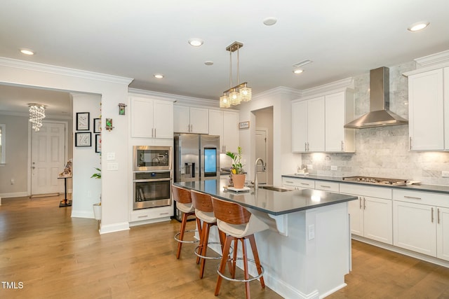 kitchen featuring sink, an island with sink, pendant lighting, stainless steel appliances, and wall chimney range hood