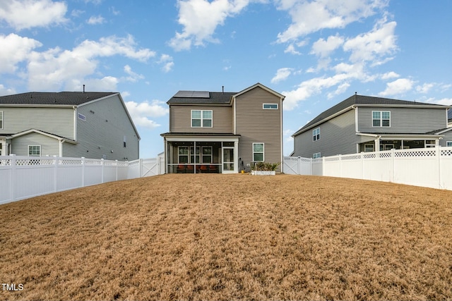 back of property with a yard, a sunroom, and solar panels