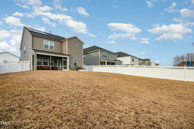 rear view of house featuring a yard, a sunroom, and solar panels