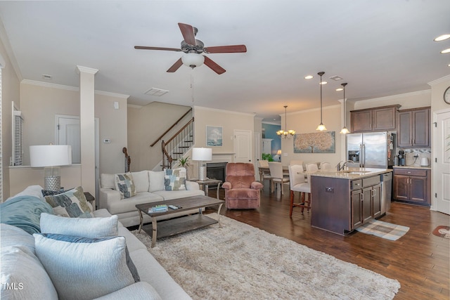 living room with dark hardwood / wood-style flooring, sink, ceiling fan with notable chandelier, and ornamental molding