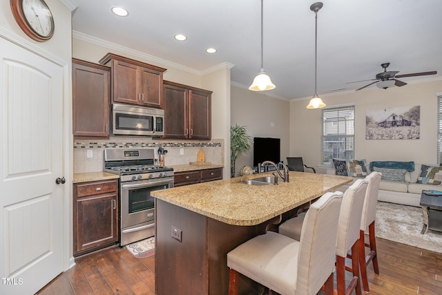 kitchen featuring sink, dark hardwood / wood-style floors, pendant lighting, stainless steel appliances, and a kitchen island with sink