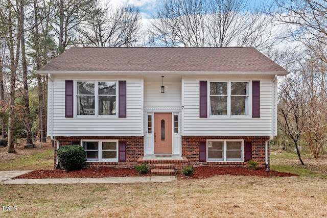 bi-level home featuring brick siding, roof with shingles, and a front yard