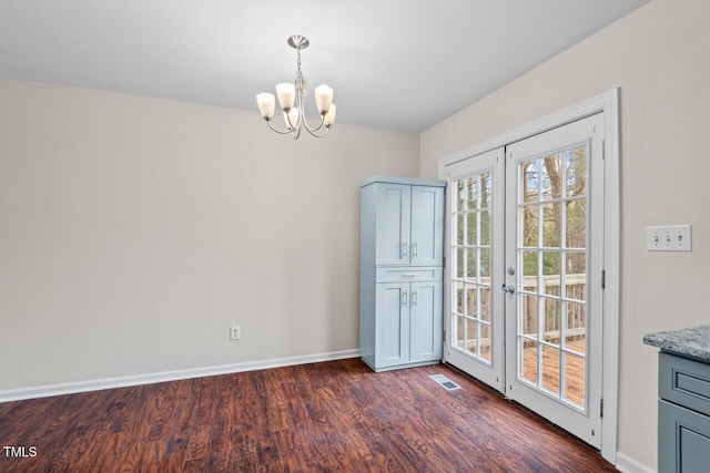 unfurnished dining area featuring dark wood-type flooring, a chandelier, visible vents, and baseboards