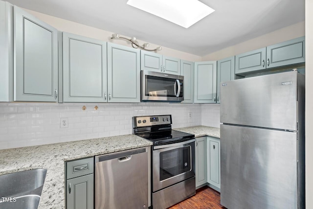 kitchen with light stone counters, stainless steel appliances, dark wood-type flooring, a skylight, and backsplash