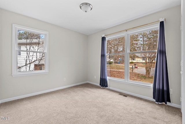 spare room featuring a wealth of natural light, carpet, visible vents, and baseboards