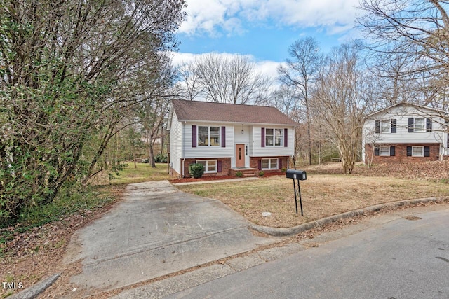 raised ranch with a front yard, concrete driveway, and brick siding