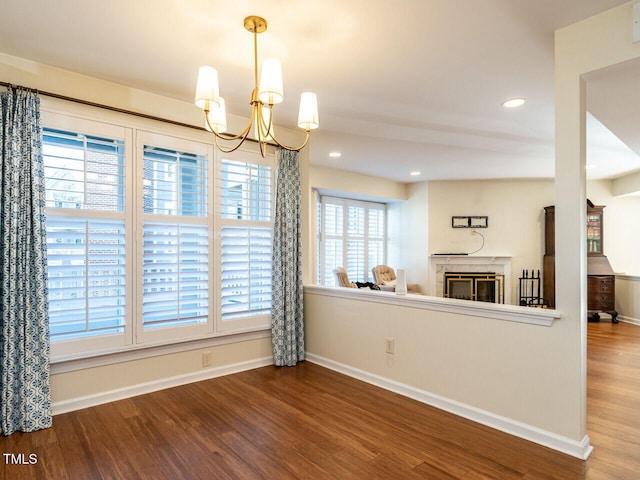 interior space with a glass covered fireplace, an inviting chandelier, baseboards, and wood finished floors