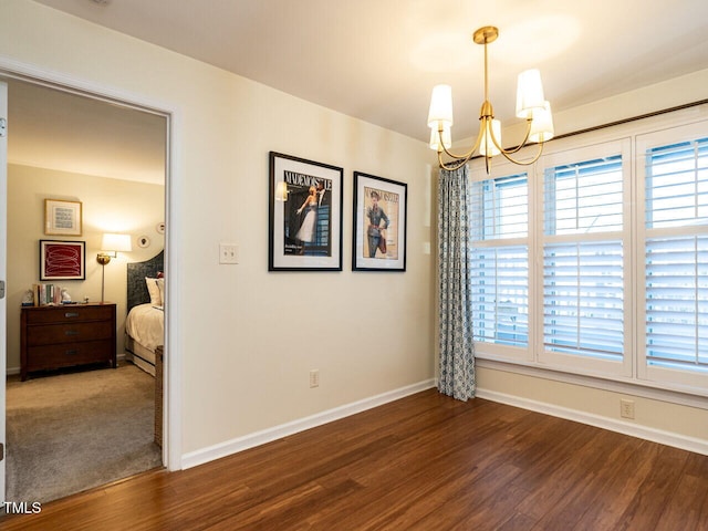 spare room with a healthy amount of sunlight, an inviting chandelier, and dark wood-style flooring