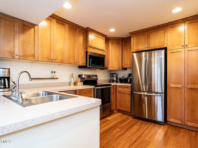 kitchen with a sink, light wood-style floors, light countertops, appliances with stainless steel finishes, and brown cabinets