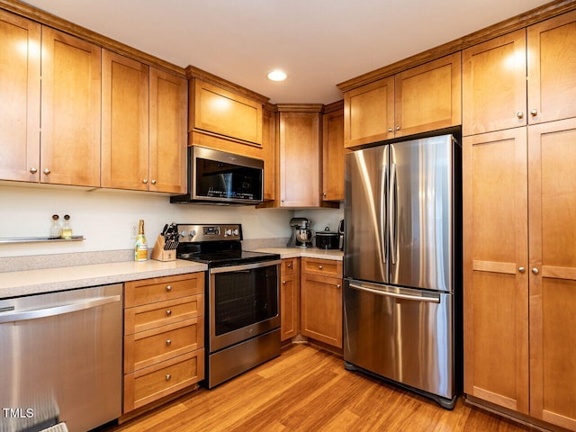 kitchen with brown cabinets, light wood-type flooring, stainless steel appliances, and light countertops