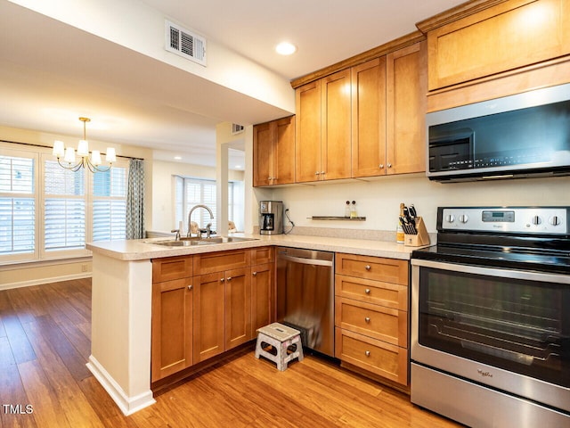 kitchen featuring visible vents, a peninsula, stainless steel appliances, light countertops, and a sink