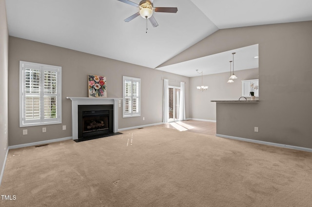 unfurnished living room featuring light carpet, baseboards, lofted ceiling, a fireplace with flush hearth, and ceiling fan with notable chandelier