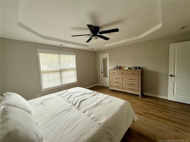 bedroom with ceiling fan, dark hardwood / wood-style flooring, and a raised ceiling