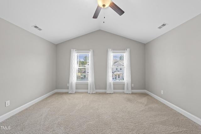 empty room featuring lofted ceiling, ceiling fan, visible vents, and light colored carpet