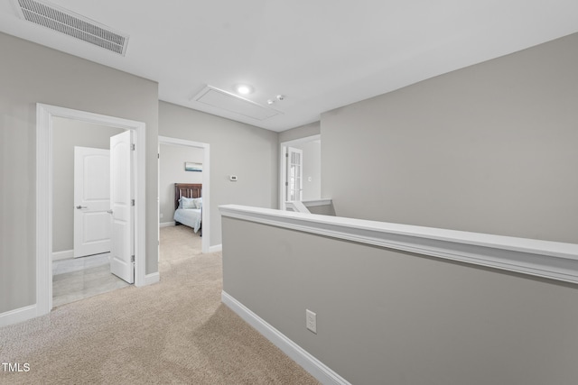 corridor with light carpet, attic access, baseboards, visible vents, and an upstairs landing