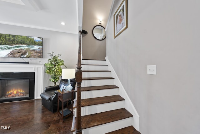 stairway with a warm lit fireplace and wood finished floors