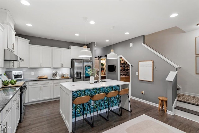 kitchen featuring appliances with stainless steel finishes, a center island with sink, hanging light fixtures, white cabinets, and a barn door