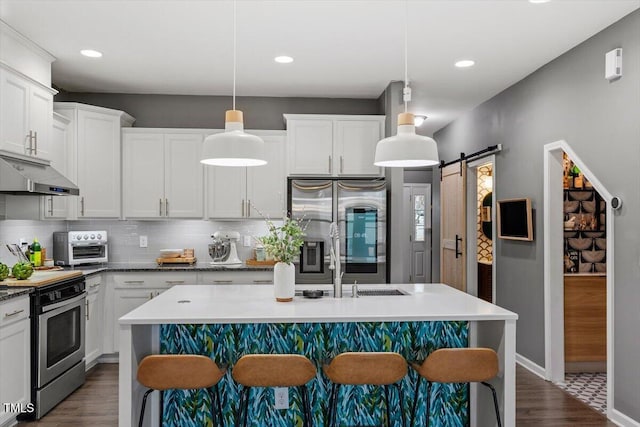 kitchen with appliances with stainless steel finishes, a barn door, pendant lighting, and a center island with sink