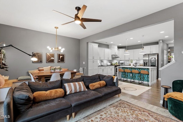 living room with light wood-type flooring and ceiling fan with notable chandelier