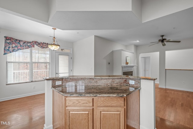 kitchen with dark stone countertops, hanging light fixtures, light hardwood / wood-style floors, and a kitchen island
