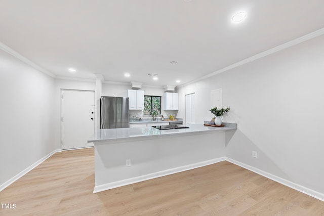 kitchen featuring light countertops, light wood-style flooring, freestanding refrigerator, white cabinets, and a peninsula