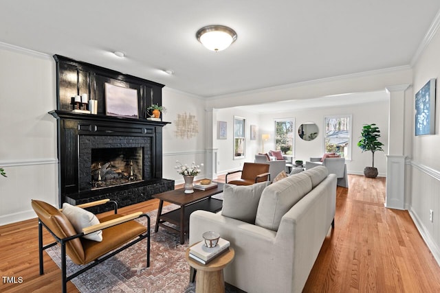 living room featuring a wainscoted wall, ornamental molding, ornate columns, a brick fireplace, and wood finished floors