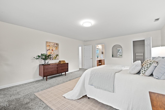 carpeted bedroom with ensuite bathroom, baseboards, a spacious closet, and visible vents