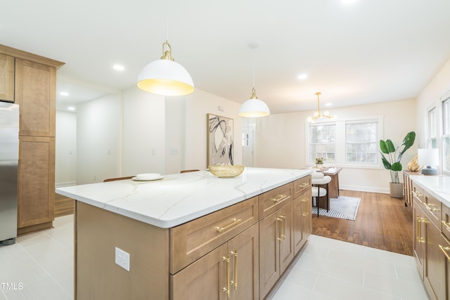 kitchen featuring light tile patterned floors, stainless steel refrigerator, a center island, light stone countertops, and decorative light fixtures