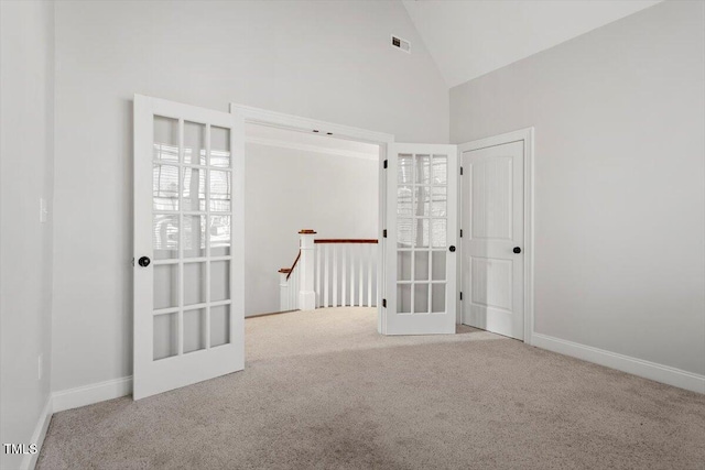 empty room featuring high vaulted ceiling, light colored carpet, visible vents, and baseboards