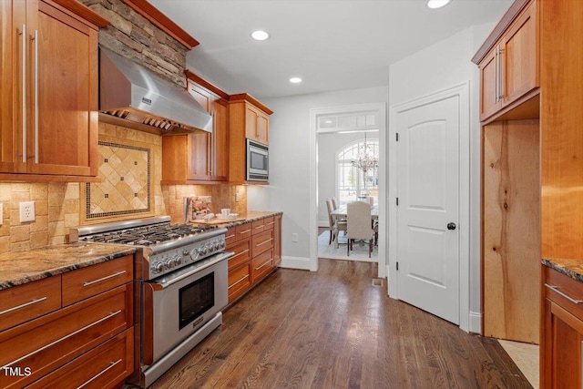 kitchen with light stone counters, appliances with stainless steel finishes, dark wood-style floors, wall chimney exhaust hood, and brown cabinetry