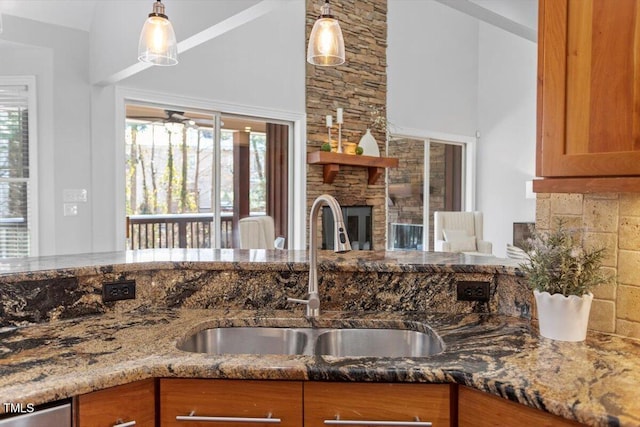 kitchen with brown cabinets, decorative light fixtures, a fireplace, stone countertops, and a sink