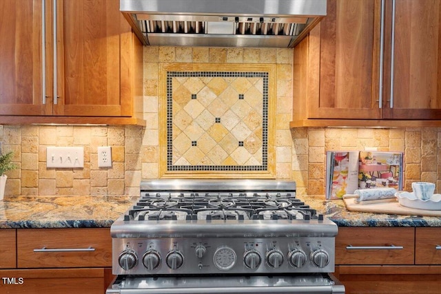 kitchen with brown cabinetry, dark stone counters, custom range hood, backsplash, and gas stove