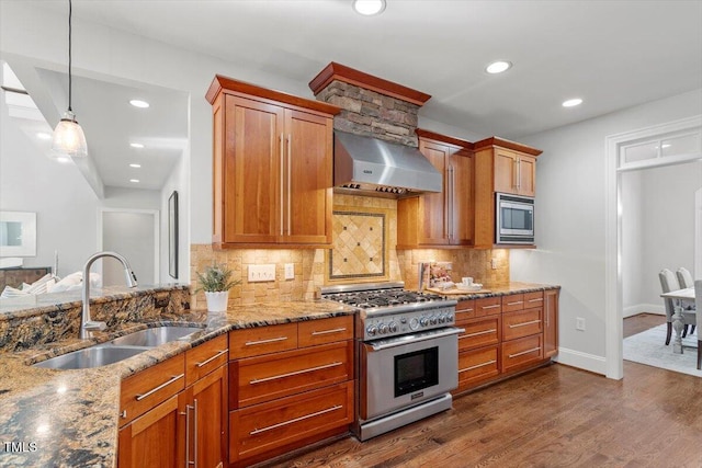 kitchen with appliances with stainless steel finishes, a sink, wall chimney range hood, and light stone countertops