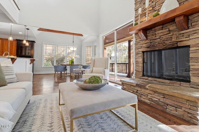 living room with a stone fireplace, a towering ceiling, baseboards, and wood finished floors