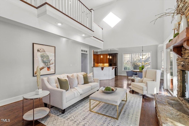 living room with a high ceiling, a skylight, wood finished floors, and baseboards