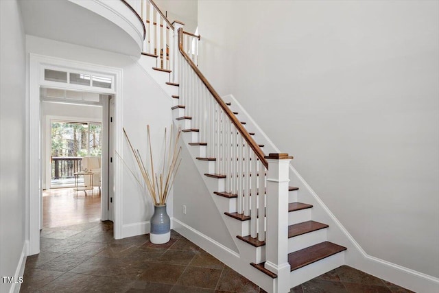 stairway featuring stone finish flooring, a towering ceiling, and baseboards