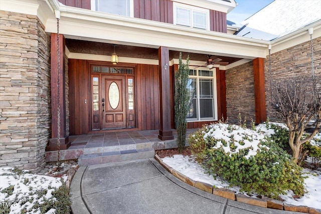 snow covered property entrance with stone siding, a porch, board and batten siding, and a ceiling fan