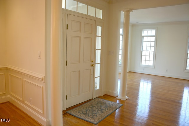 entryway featuring light wood-type flooring, wainscoting, decorative columns, and a decorative wall