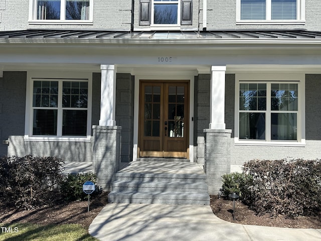 entrance to property featuring a standing seam roof, brick siding, metal roof, and french doors