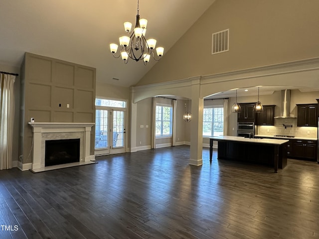 unfurnished living room with arched walkways, dark wood-style flooring, a fireplace, visible vents, and an inviting chandelier