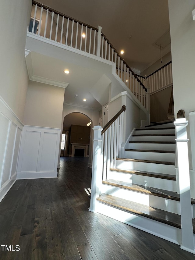 foyer entrance featuring a fireplace, a decorative wall, dark wood-type flooring, ornamental molding, and stairs