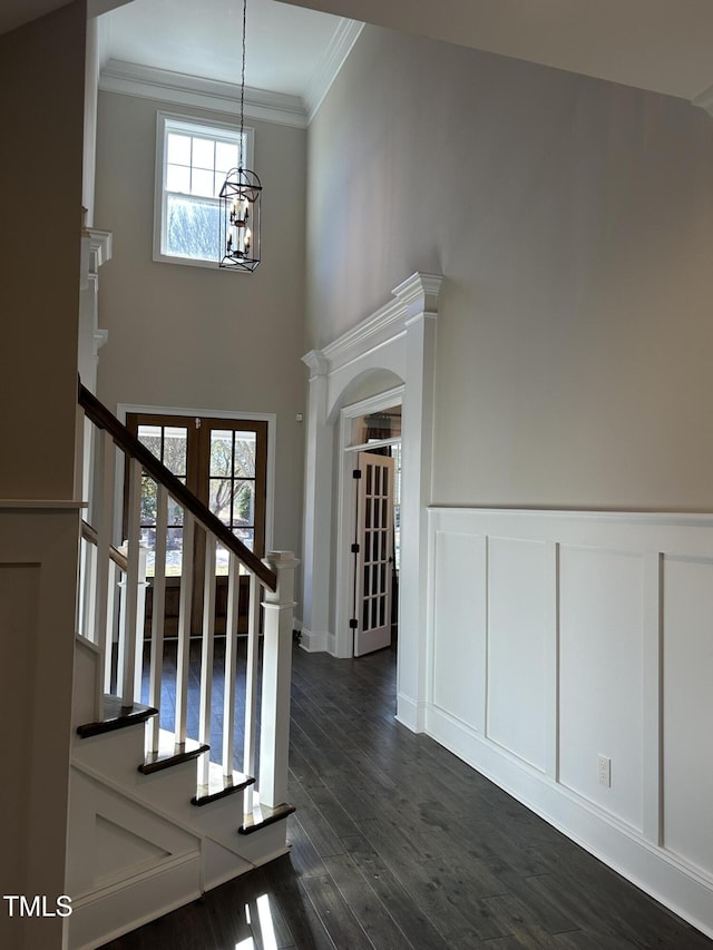 foyer featuring a decorative wall, dark wood-style flooring, ornamental molding, stairway, and wainscoting