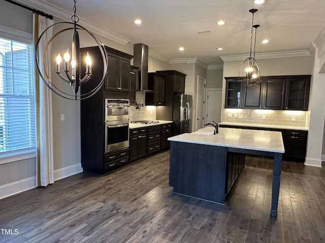 kitchen featuring a center island with sink, light countertops, appliances with stainless steel finishes, glass insert cabinets, and wall chimney exhaust hood