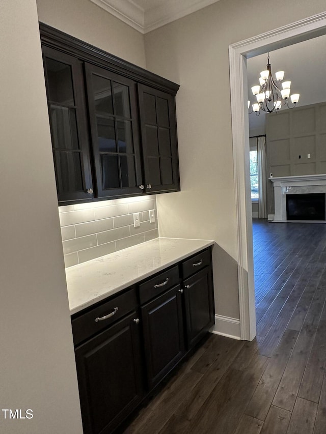 kitchen with dark wood-type flooring, baseboards, ornamental molding, backsplash, and glass insert cabinets