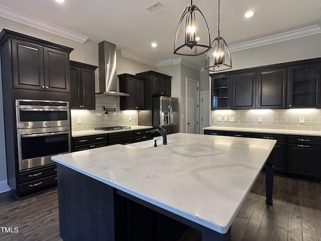 kitchen featuring wall chimney exhaust hood, visible vents, stainless steel appliances, and a large island with sink