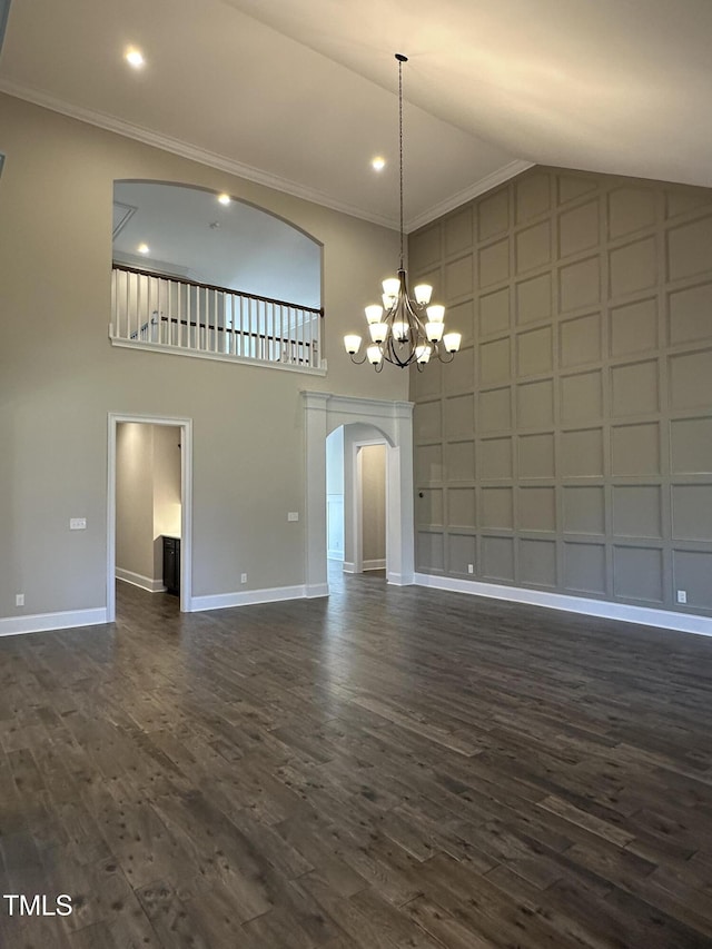 unfurnished living room featuring baseboards, arched walkways, dark wood finished floors, ornamental molding, and an inviting chandelier