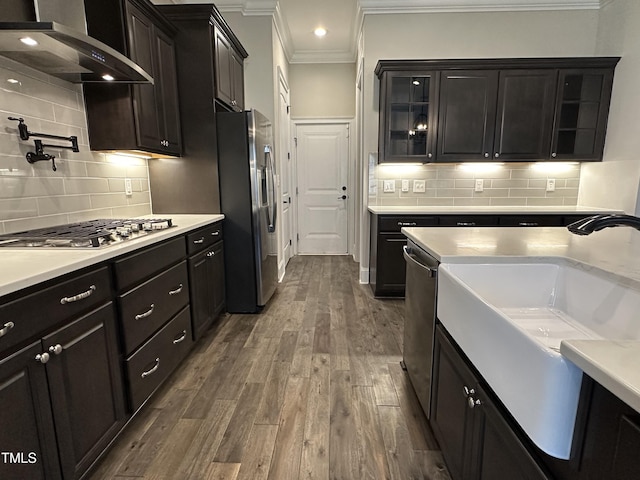 kitchen with glass insert cabinets, stainless steel appliances, light countertops, and wall chimney exhaust hood