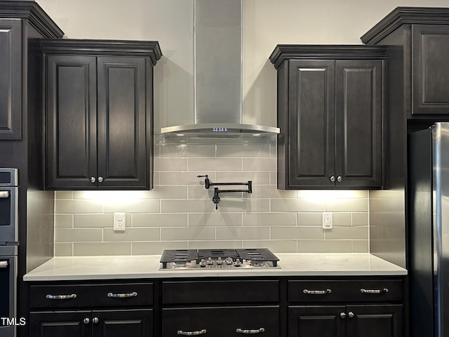 kitchen with appliances with stainless steel finishes, light countertops, wall chimney exhaust hood, and dark cabinetry