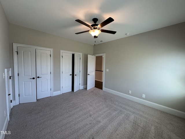 unfurnished bedroom with visible vents, baseboards, a ceiling fan, carpet floors, and two closets